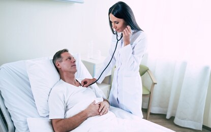 young modern confident woman doctor in a white coat with a stethoscope is examining the patient's feelings while he is lying on the bed in the hospital ward.
