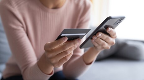 close up female hands holding credit card and smartphone, young woman paying online, using banking service, entering information, shopping, ordering in internet store, doing secure payment