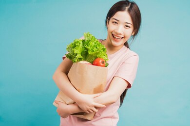 young girl holding a bag of freshly bought vegetables on a green background
