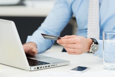 businessman doing online banking, making a payment or purchasing goods on the internet entering his credit card details on a laptop, close up view of his hands