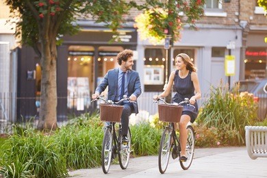 businesswoman and businessman riding bike through city park