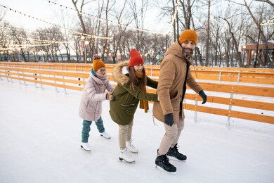 family holding to each other while skating on the rink in the park