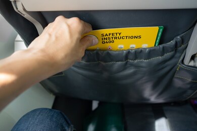 close-up of asian male's hand picking aircraft safety card or an emergency information instruction manual from the airplane seat pocket in front of him. safety card to be at every seatback on airplane