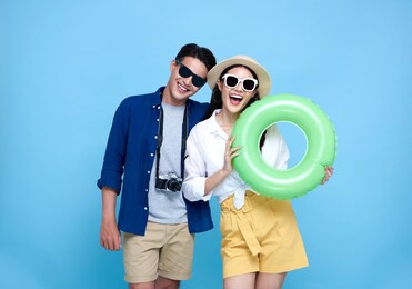 happy playful asian couple tourist dressed in summer clothes and beach accessories to travel on holidays isolated on blue background.