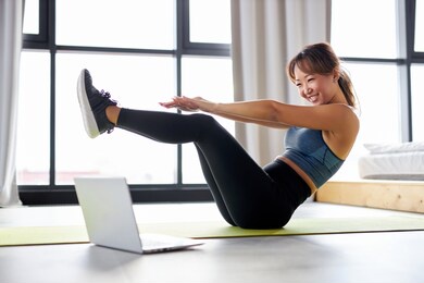 asian woman excercising at home, watching video tutorial on laptop, workout on the floor. sport online concept