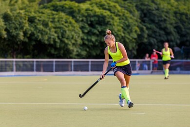 young field hockey female player in attack. sporty woman player leads the ball