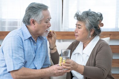 asian elderly couple, taking care of health in retirement, senior woman helping her husband take a pills or vitamin pills at home.