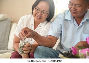 elderly couple put coins in a glass jar to save money.