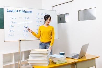 asian female teacher teach chinese language for foreign online through laptop in classroom