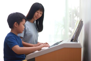 asian mother teaching her son playing electronic organ at home.
