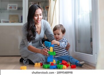 young asian woman playing colorful plastic blocks with little baby at home or nursery room. happy family mother and son play and learn with developing toy together.