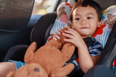 adorable asian kid boy (toddler age 1-year-old) protection sitting in the car seat with safety belt locked and holding bear doll. journey baby careful concept. portrait closeup and blurry background.
