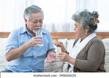 asian elderly couple, taking care of health in retirement, senior woman helping her husband take a pills or vitamin pills at home.