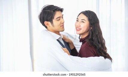 young asia couple together hugging under white blanket. romantic couple on a winter holiday. man and woman standing together in bed room wrapped in blanket. couple embracing and smiling.