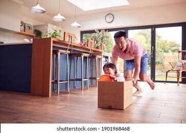 asian father and son pushing son around kitchen floor at home in junk modelled car