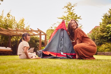 asian mother with daughter in garden at home putting up tent for camping trip together