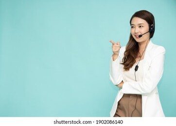 portrait of happy smiling asian woman customer support phone operator and pointing to empty copy space isolated on green background, call center or customer service concept