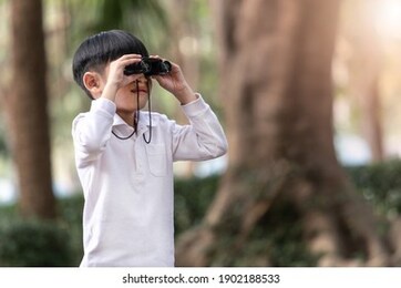little asian boy looking through binoculars in the forest. the child was watching binoculars in nature outdoor.