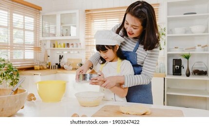 happy smiling young asian japanese family with preschool kids have fun cooking baking pastry or pie for breakfast meal in modern kitchen home in the morning. doing bakery knead dough and bake cookies.