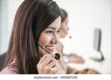 portrait of beautiful asian woman sitting smiling and wearing headset working customer support and assistance service call center in workplace at office. business call center and hot line operators.