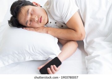 the young man is sleeping on the bed with the phone still in his hand