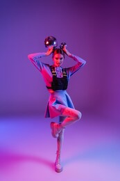 full length of stylish woman in skirt holding disco balls on purple