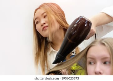 the pretty asian hairdresser dry and style hair of young girl in the barber shop