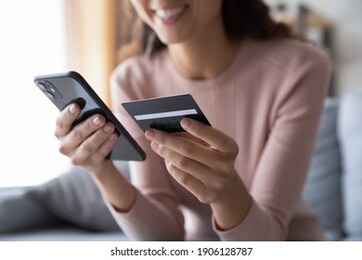 close up smiling millennial woman holding smartphone and banking credit card, involved in online mobile shopping at home, happy female shopper purchasing goods or services in internet store.