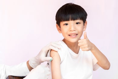 a happy smiling kid while being vaccinated. doctor vaccinating little asian boy is thumbs up. doctor examining a child in a hospital.