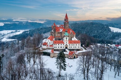 castle in winter. romantic fairytale castle in picturesque highland landscape, covered in snow. castle with white church, high towers, red roofs, stone walls. bouzov castle, czech republic.
