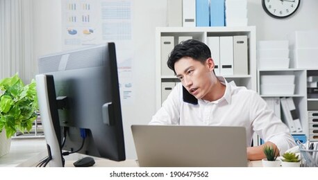 asian young business man speak on smartphone and use computer to discuss his work plan in the office