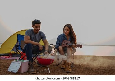 young asian couple grilling barbecue in front of tent while camp