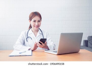 portrait of asian doctor woman happy smiling working clinical hospital office work desk background. medical healthcare professional worker provider service, contacting mobile smart phone technology 