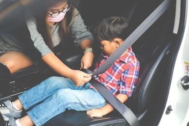 asian fat woman fastening child with safety seat belt in car.