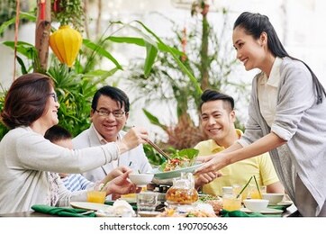 young beautiful asian woman offering tasty salad to guests at family dinner