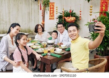 happy middle-aged vietnamese man taking selfie with his big family at lunar new year celebration