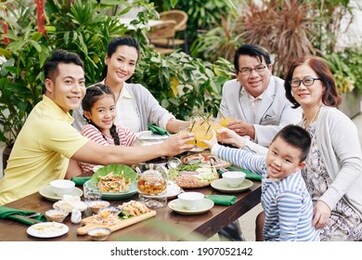 big happy asian family toasting with glasses of orange juice when sitting at big dinner table and celebrating spring festival