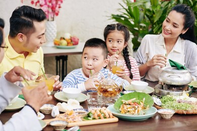 parents and children drinking juice and eating traditional vietnamese dishes at family dinner