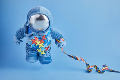 world autism awareness day background. blue plush astronaut toy with puzzle heart, autism symbol, on blue background