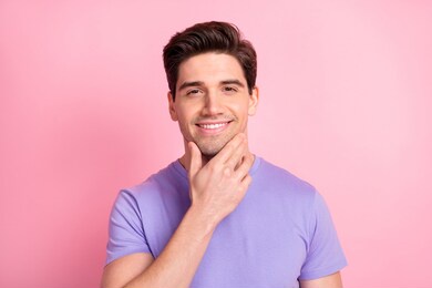 portrait of attractive cheerful content groomed guy touching chin isolated over pink pastel color background