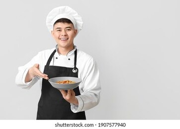 handsome asian chef with dish on grey background