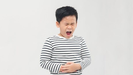 sad little asian boy suffering from stomach ache, holding his stomach, isolated on white background.