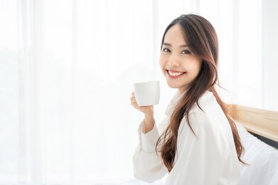 young asian woman sitting on bed at home and drinking milk after wake up in the morning