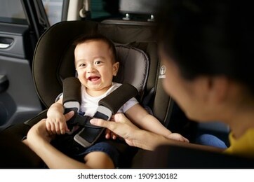 asian little baby happy and fun while fastened belt and seat in the safety car seat. a boy looking his mother and smile in a car. 