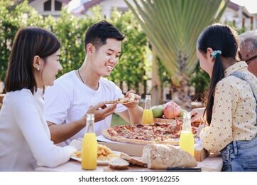 happy asian family having enjoying meal(pizaa, salad,snack, orange juice) together in home garden. outdoor dinner party in holiday. multi generation family concept.