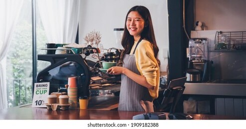 young asian woman barista wear apron making coffee cup served to customer at bar counter in coffee shop with smile face.concept of cafe and coffee shop small business.vintage tone