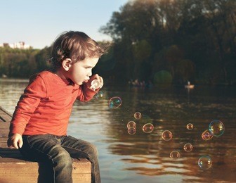 little boy blowing soap bubbles at a lake