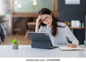 image of an asian woman who is tired and overthinking from working with a tablet at the office.