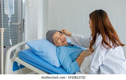 older asian woman patient covered the head with clothes effect from chemo treatment in cancer cure process talking to a female doctor.