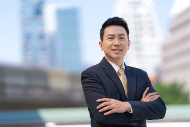 portrait of successful asian businessman standing with arms crossed standing in front of modern office buildings